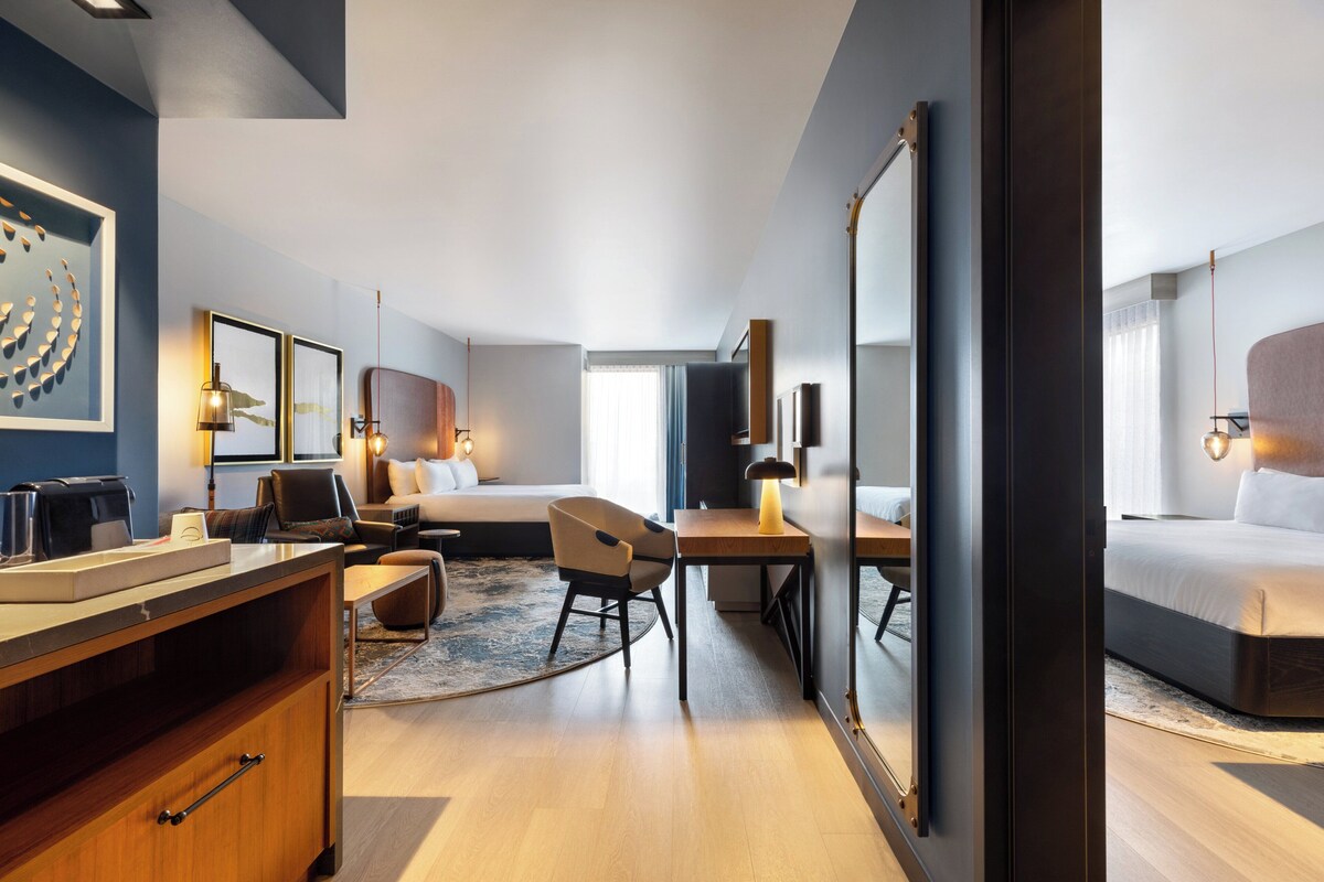 A modern hotel room with a large bed, a desk, a chair, and a large mirror.