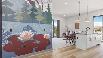 A modern kitchen with a large island, pendant lights, and a mural with trees and water lilies.