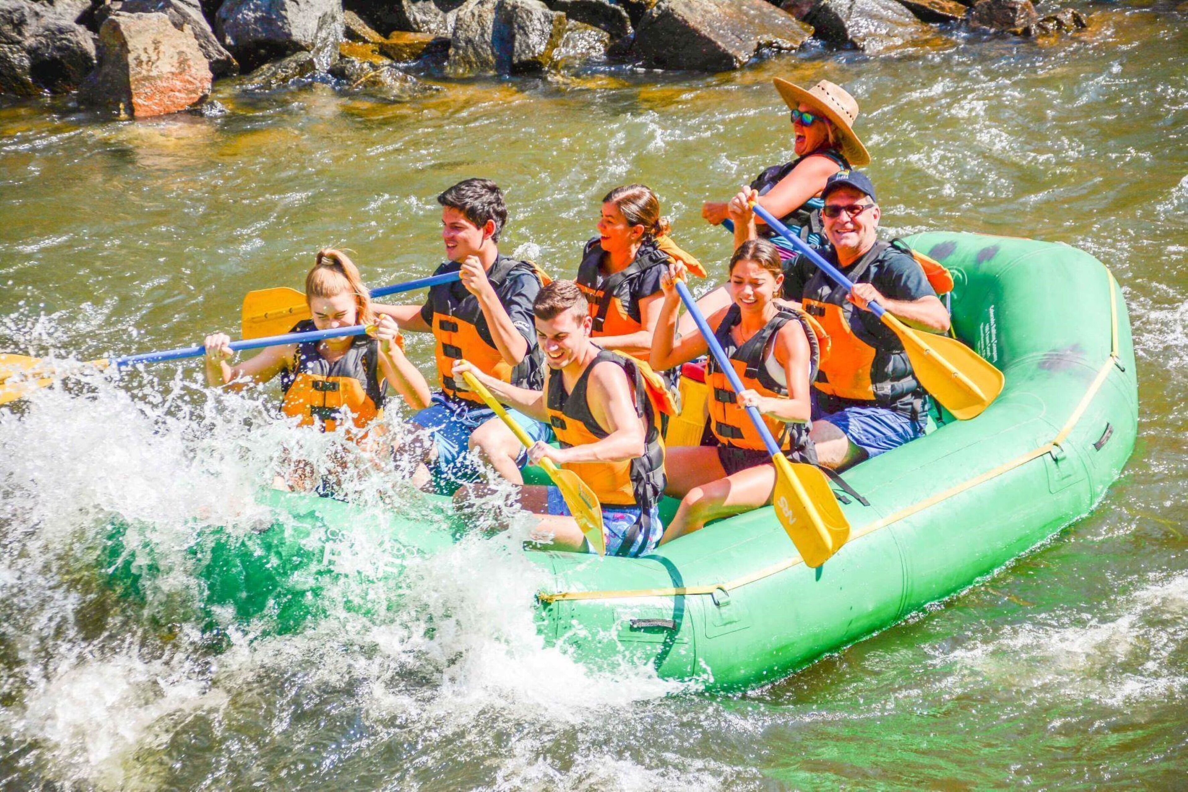 A group of people in a green inflatable raft navigating a river with rapids.