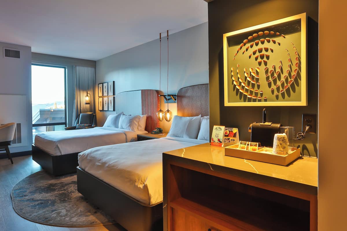 Habitación de hotel con dos camas, un escritorio de madera, un espejo grande y vistas al exterior.