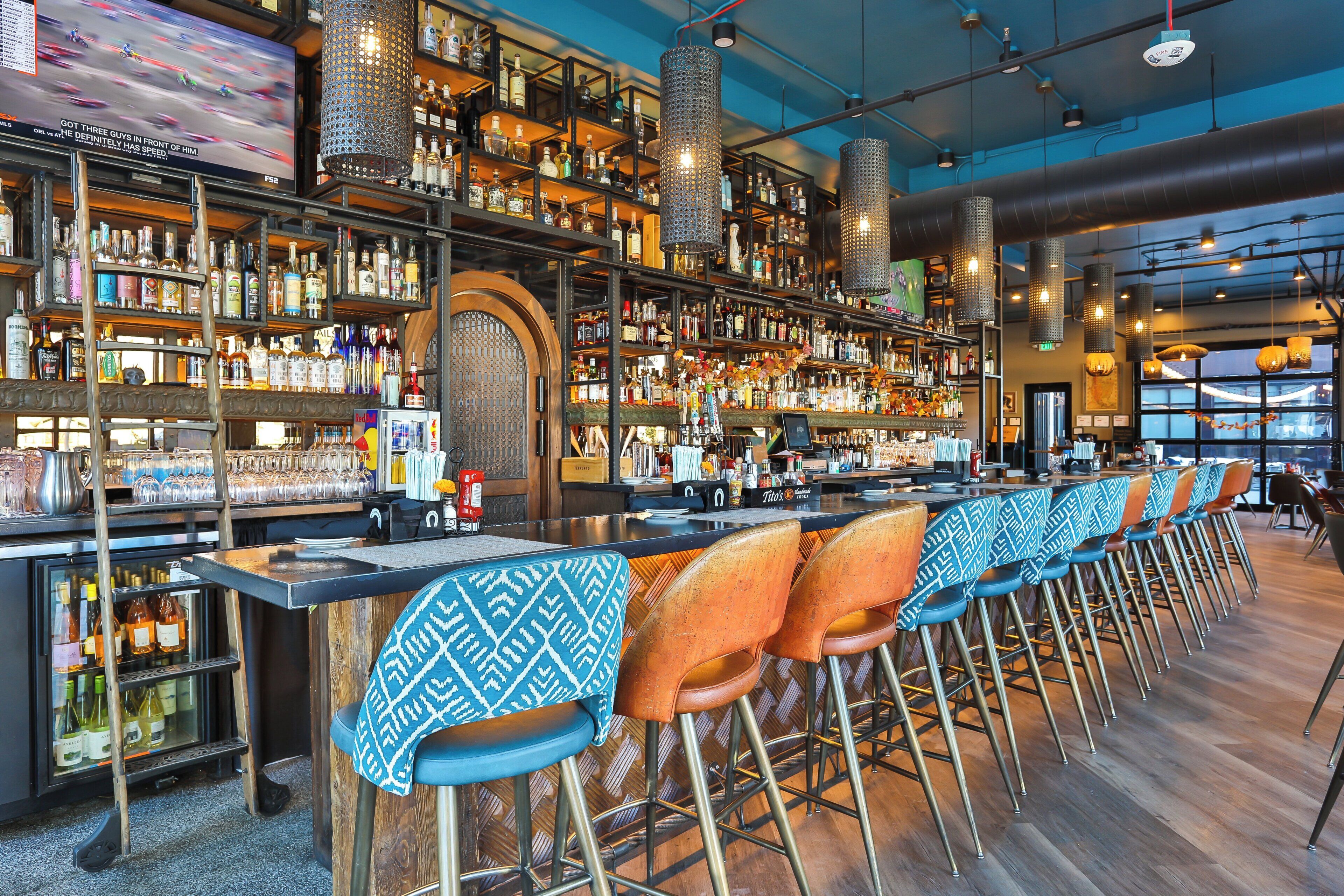 A bar area with multiple seating options, a variety of liquor bottles on shelves, and a television screen displaying a sports event.