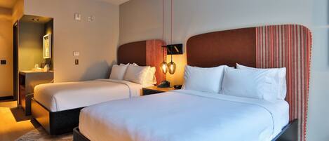 A hotel room with two beds, a nightstand with a lamp, a mirror, and a small table.