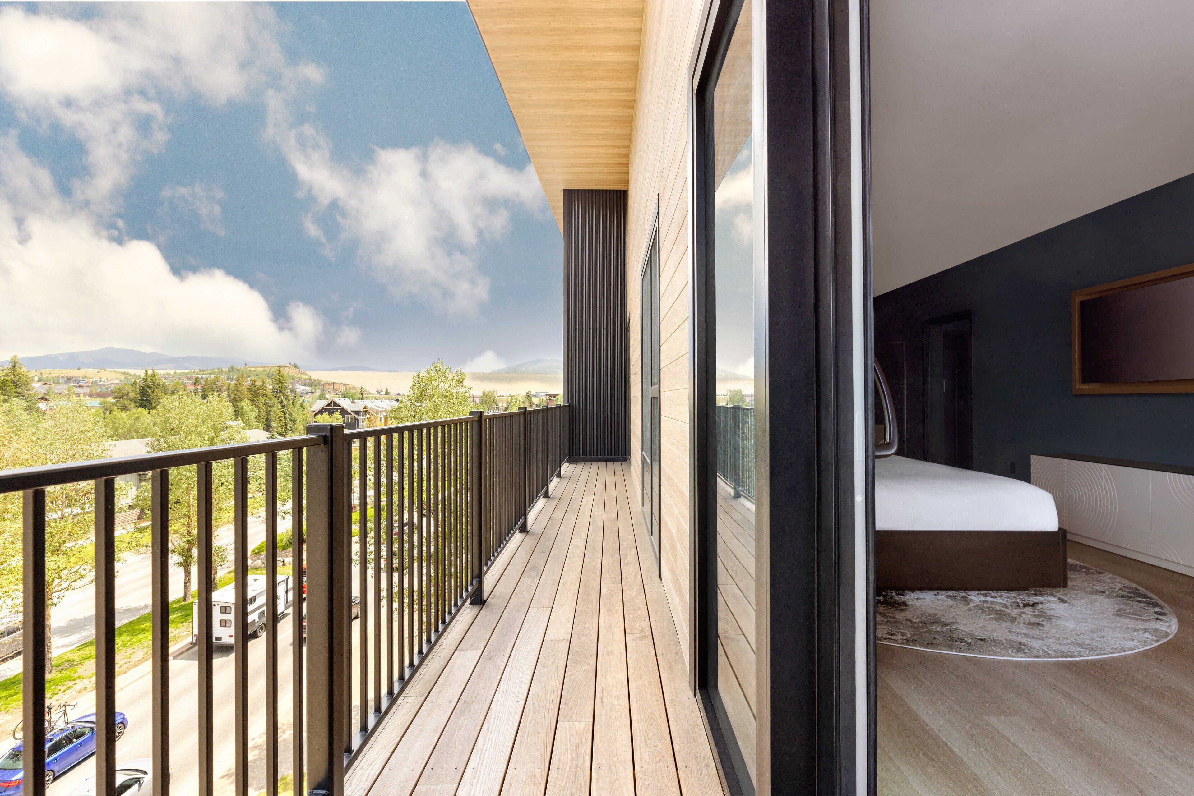 A balcony with a wooden floor and black railing, overlooking a road and greenery.