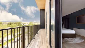 A balcony with a wooden floor and black railing, overlooking a road and greenery.