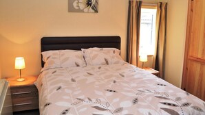 A neatly made bed with a floral-patterned bedspread, a bedside lamp, and a wall-mounted painting of flowers. - Character former shepherds cottage for couples or young families. (near Bootle)