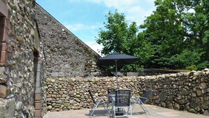 A patio area with stone walls, a potted plant, and outdoor furniture. - Character former shepherds cottage for couples or young families. (near Bootle)