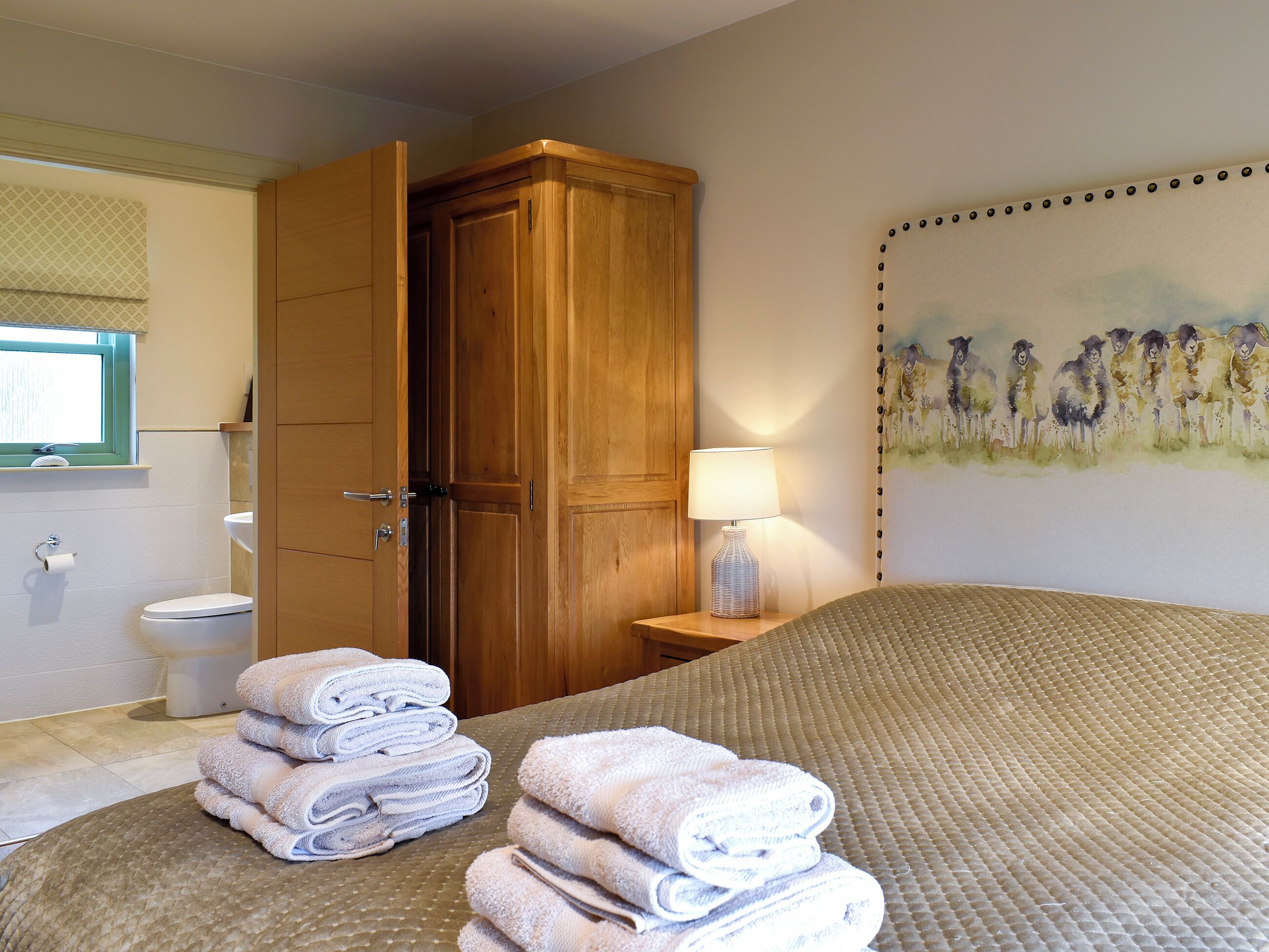 A hotel room with a bed, a wooden wardrobe, a bathroom with a toilet, and a painting on the wall.