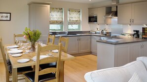 A modern kitchen with wooden cabinetry, a dining table set for four, and a kitchen island with appliances. - 3 bedroom accommodation in Linlithgow, near Edinburgh (Linlithgow, near Edinburgh)