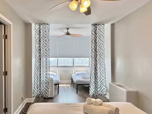 A hotel room with a bed, two bedside tables, a ceiling fan, and a window with blinds.
