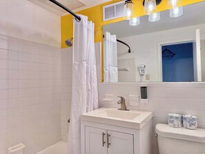 A bathroom with white tiles, a shower curtain, a sink with a faucet, and toilet paper on the tank.