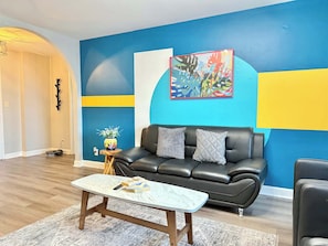 A living room with a black leather sofa, a marble coffee table, and a colorful abstract painting on the wall.