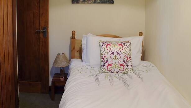 A neatly made bed with a green blanket, a wooden headboard, and a decorative pillow.