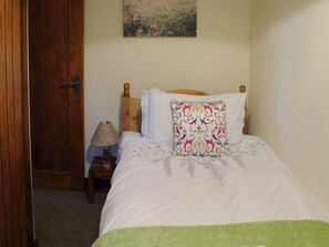 Ein ordentlich bezogenes Bett mit einer grünen Decke, einem hölzernen Kopfteil und einem Zierkissen.