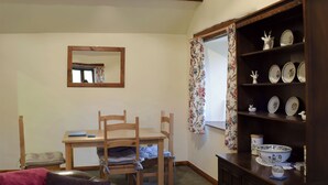 A cozy room with a wooden dining table, chairs, a sofa, a cabinet with decorative plates, and a mirror on the wall.