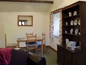 Una habitación acogedora con una mesa de comedor de madera, sillas, un sofá, un aparador con platos decorativos y un espejo en la pared.