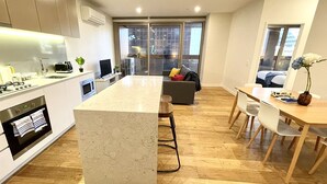 Una cocina moderna con una isla central, un comedor con mesa y sillas de madera, y una sala de estar con sofá y televisor.
