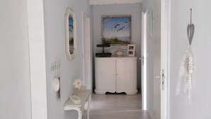 A hallway with a white door, a white cabinet, a small table with a vase, a mirror, and a painting of birds. - Lüttje Fehn - Ostfriesische Idylle (Uplengen)