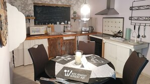 A dining area with a table set for two, a kitchen with modern appliances, and a chalkboard with a welcome message. - Lüttje Fehn - Ostfriesische Idylle (Uplengen)