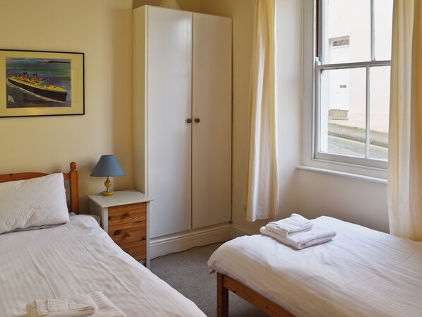 A hotel room with two beds, a wardrobe, a bedside table with a lamp, and a window with curtains. - CHURCH ST 1 UPPER APARTMENT (Buckley St)