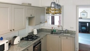 Cocina compacta con estufa a gas, microondas y pileta. Se observa una ventana con cortinas y un panel decorativo sobre la pileta.
