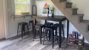 Eine Küche mit einer Holztreppe, einem Fenster mit Jalousien, einer Bar und einem kleinen Regal mit Pflanzen und Dekoration.