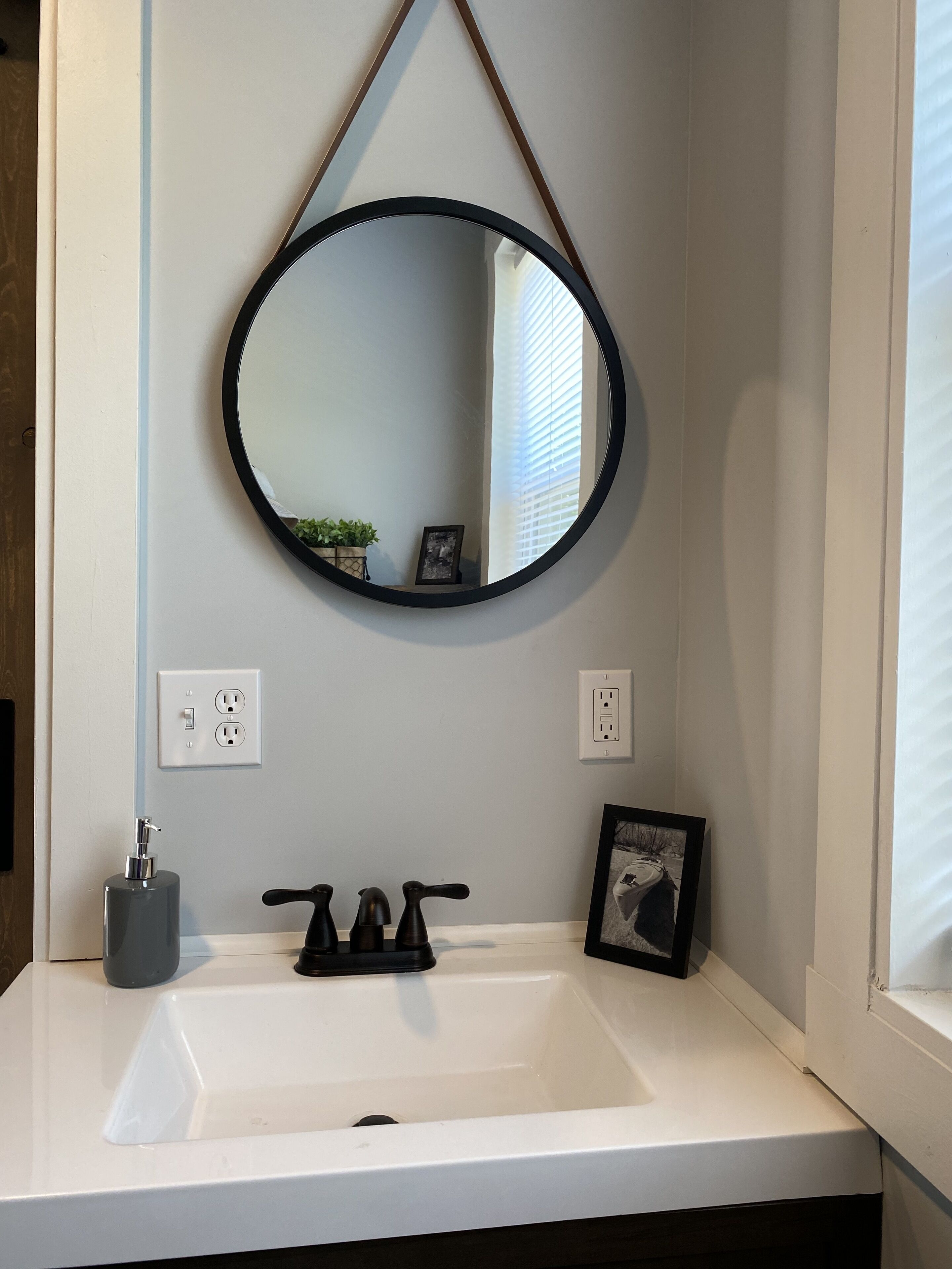 A bathroom with a white sink, black faucets, a round mirror, and a framed picture on the wall.