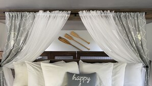 Ein Bett mit grauer Bettwäsche, weißen Kissen und einem grauen Kissen mit dem Aufdruck "happy place". An der Wand über dem Bett befinden sich Holzschilder.