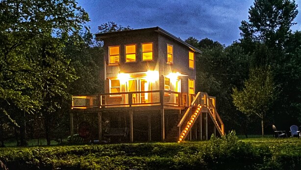 Ein zweistöckiges Haus mit Balkon und Treppe, das sich im Wasser spiegelt.