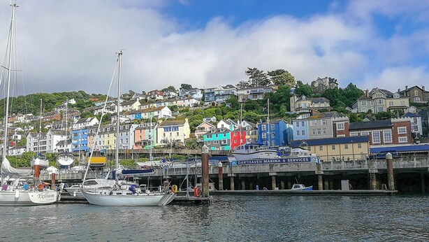 Un port où des bateaux sont amarrés, une enseigne indiquant « Darthaven Marina & Services », et des bâtiments aux couleurs vives en arrière-plan.
