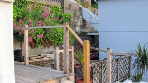 Une terrasse en bois avec une table dressée pour le thé, entourée de plantes en pot et d’une clôture en bois.