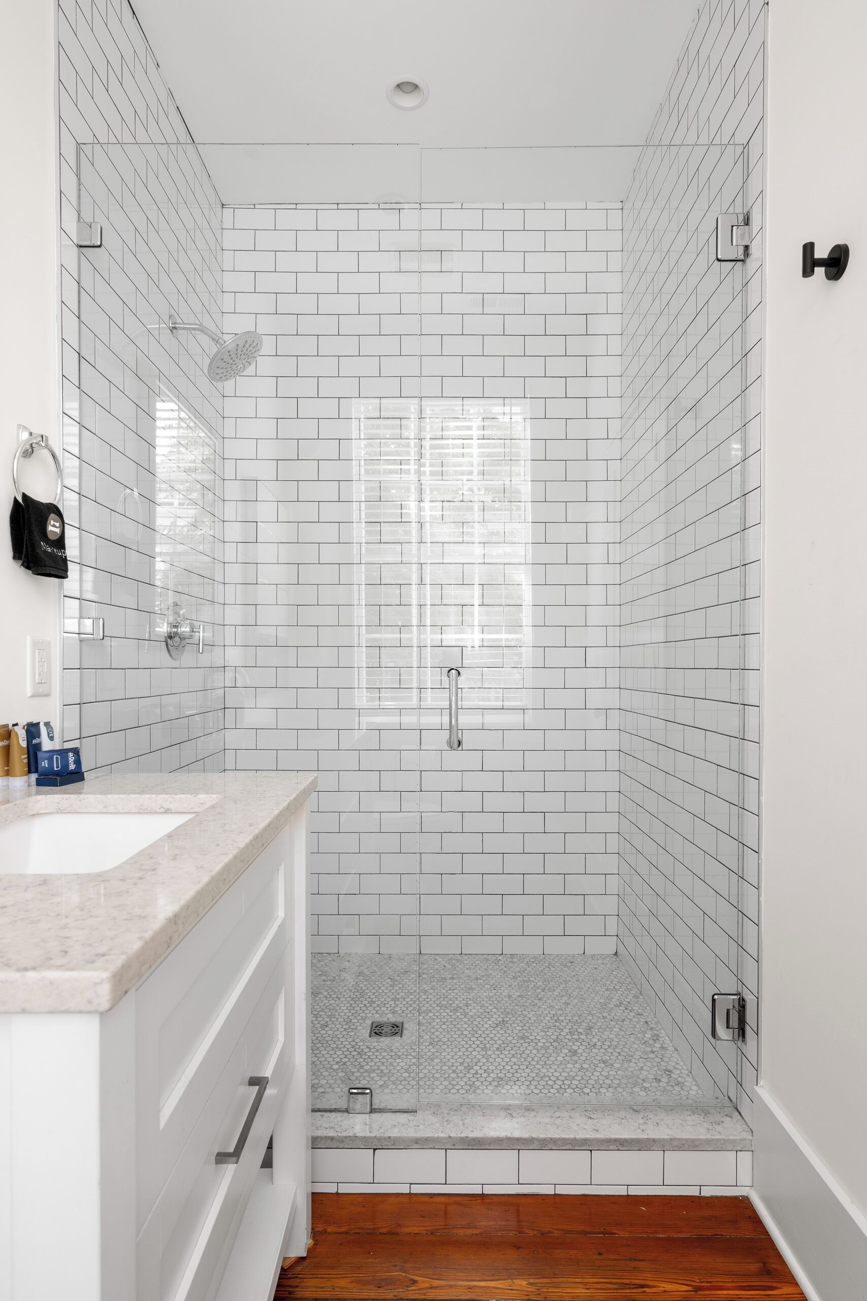 A bathroom with white subway tiles, a shower with a glass door, and a wooden floor.
