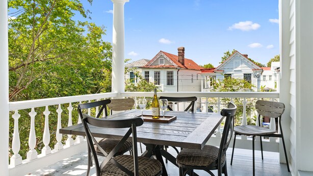 A covered porch with a wooden table and chairs, a bottle of wine, and a tray.