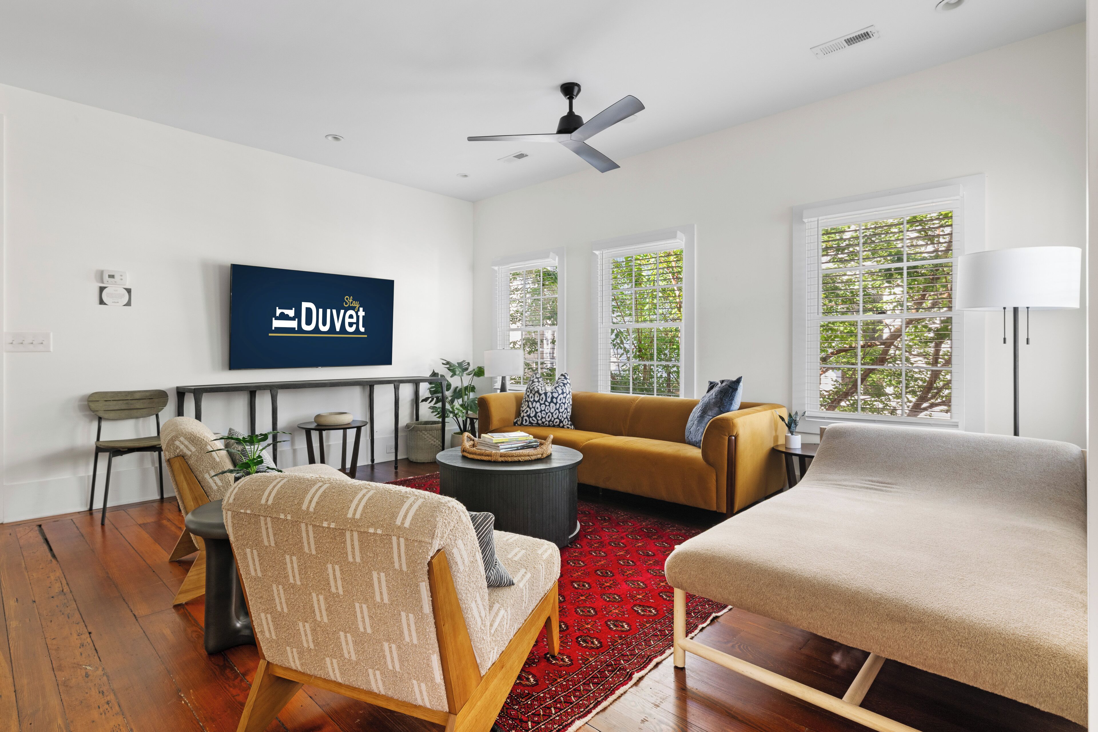 A modern living room with a sofa, chairs, a coffee table, and a television displaying 'Duvet.'