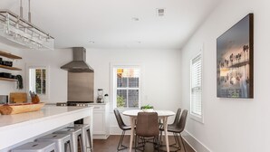 A modern kitchen with a central island, bar stools, and a dining table with chairs. - Private Pool! | Rooftop Patio | The Athena (Charleston)