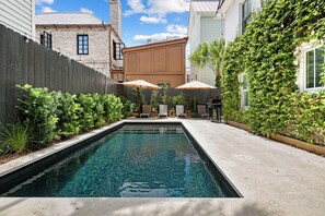 A rectangular swimming pool with a wooden fence on one side and a building with a brick facade on the other. - Private Pool! | Rooftop Patio | The Athena (Charleston)