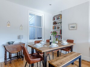A dining area with a wooden table, chairs, and a bookshelf in the background.