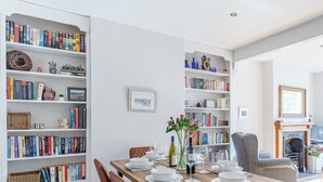A dining area with a wooden table set for four, surrounded by bookshelves filled with books and decorative items. - 3 bedroom accommodation in Dartmouth (Dartmouth)