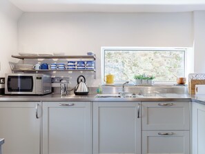 Een moderne keuken met een RVS magnetron, waterkoker en nog een waterkoker op het aanrecht. Er is een raam met uitzicht op groen.
