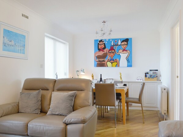 A modern living room with a beige sofa, a dining table with chairs, a chandelier, and a painting on the wall. - 4 bedroom accommodation in Maryport (Maryport)