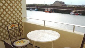 Un balcone con due tavoli e sedie rivestiti di mosaici, affacciato su un porto con barche.