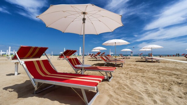 Una playa con hileras de sillones rojos y blancos a rayas y sombrillas blancas.
