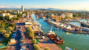 Un puerto deportivo con barcos amarrados, una carretera al borde del agua y edificios al fondo.