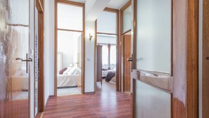 Un pasillo con piso de madera y puertas que dan a un dormitorio con cama y ventana.