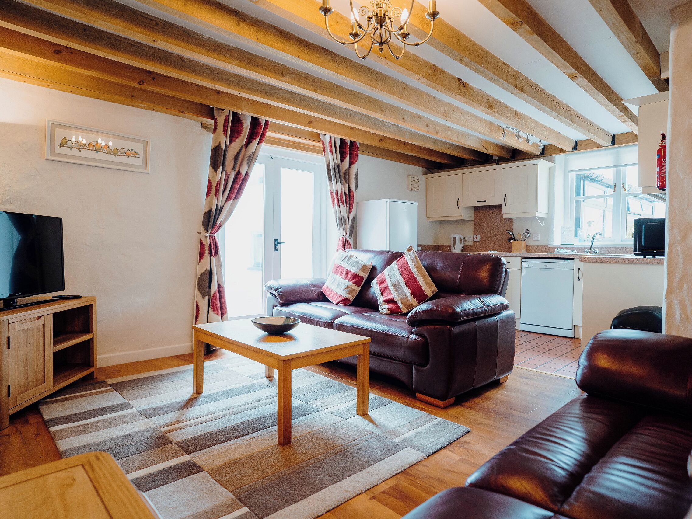 A living room with a sofa, a coffee table, a television, and a kitchen in the background.