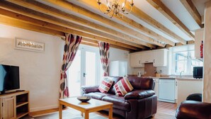 A living room with a sofa, a coffee table, a television, and a kitchen in the background. - St David's Lodge - UK6738 (Lydstep, near Tenby)