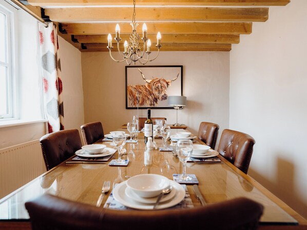 A dining room with a wooden table set for six, a chandelier, and a framed animal picture on the wall.