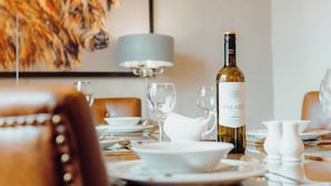 A dining table set with plates, glasses, a wine bottle, and a dog in the background. - St David's Lodge - UK6738 (Lydstep, near Tenby)