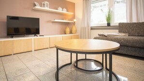 Een moderne woonkamer met een ronde tafel, een bank, een televisie en planken met decoratieve objecten.