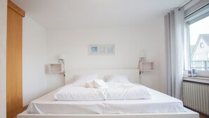 Een minimalistische slaapkamer met een groot bed, witte beddengoed, twee nachtkastjes en een ingelijst schilderij aan de muur.