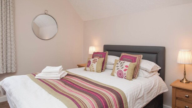 A neatly made bed with a striped blanket, two bedside lamps, and a round mirror on the wall.